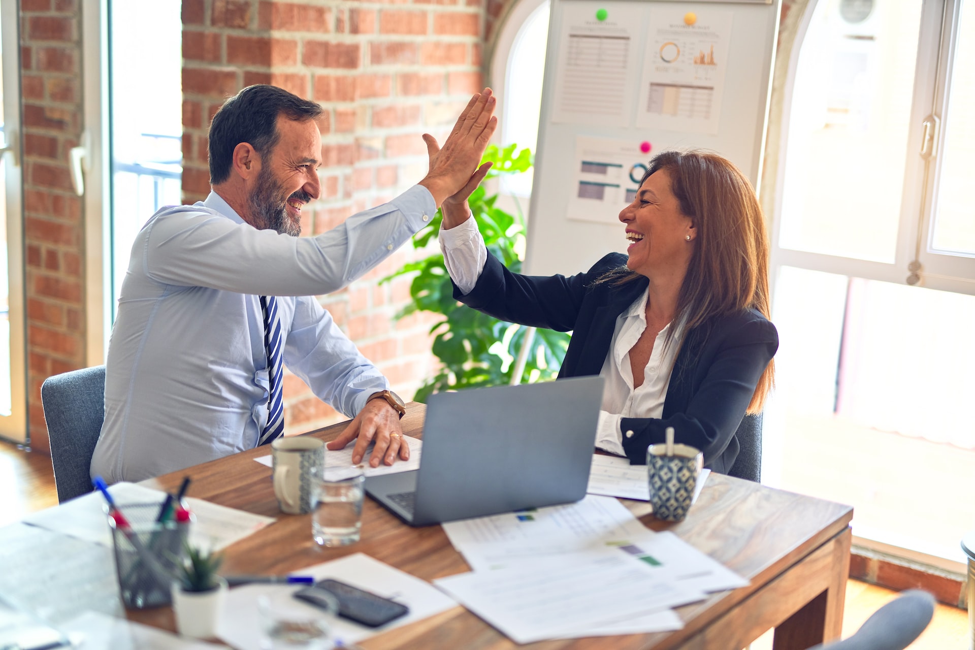 Two coworkers high-fiving over a table full of paperwork